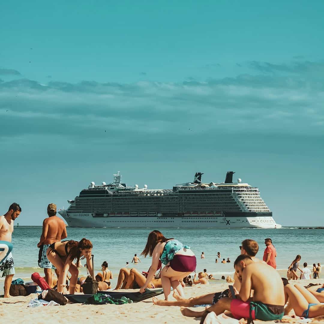Beachgoers enjoying the sun with a cruise ship on the horizon